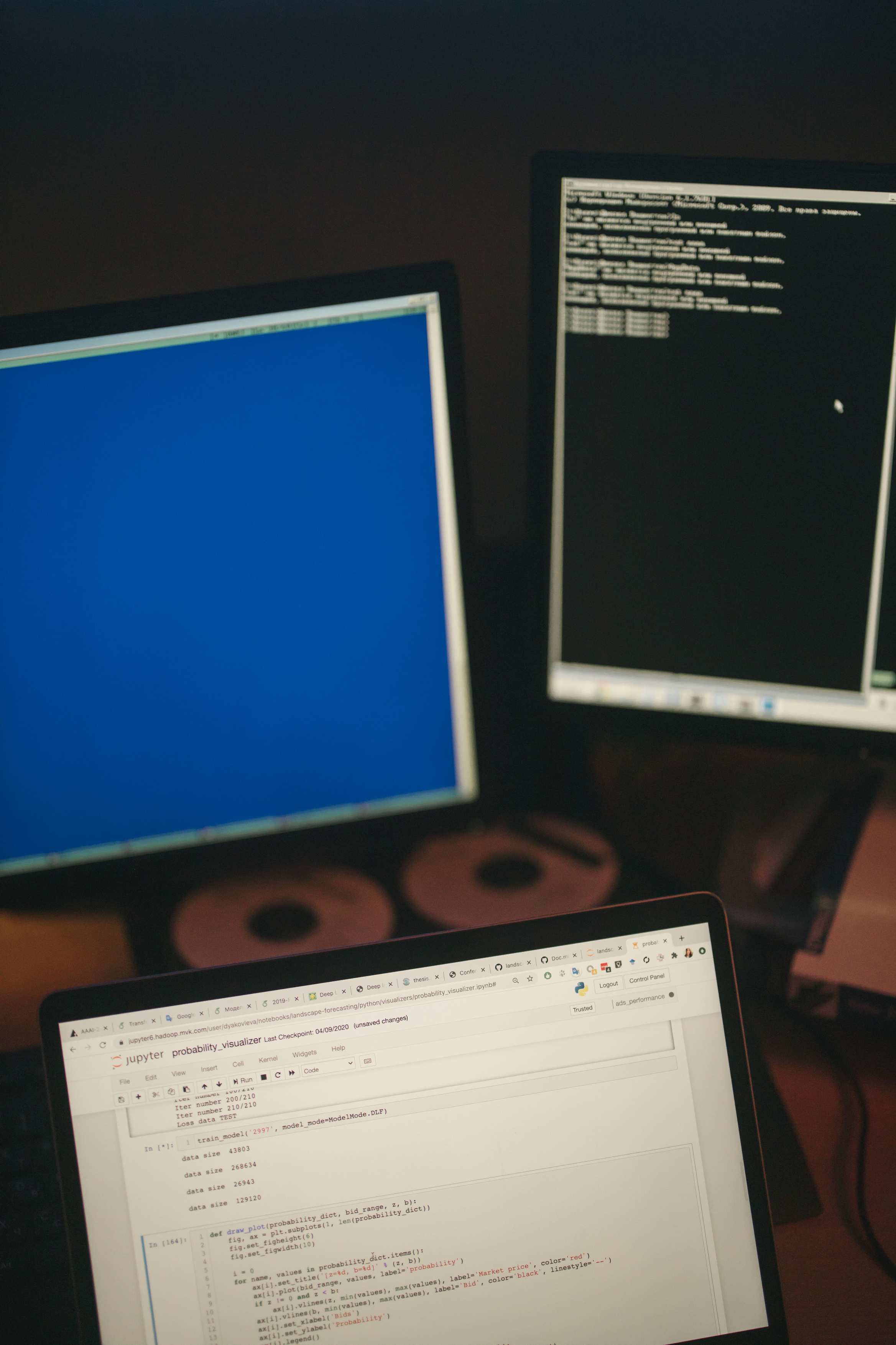 Close view of a computer monitor showing code beside a keyboard on a multi-screen workstation